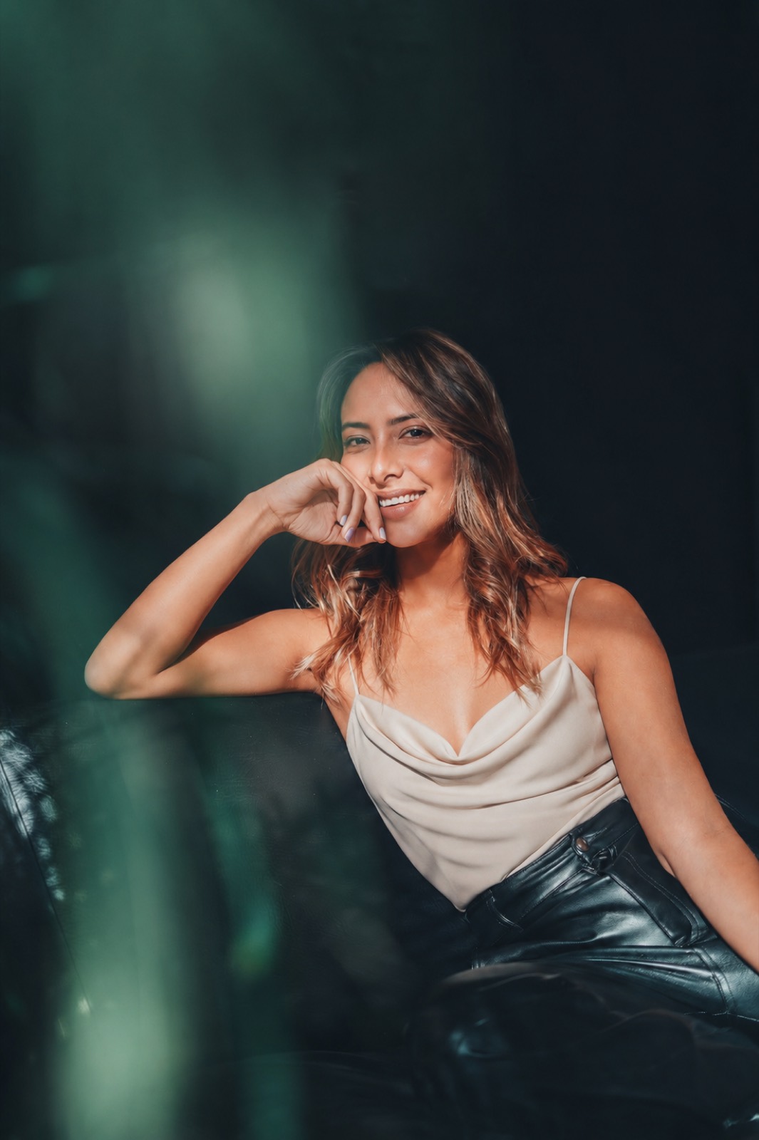 Portrait of Luisa Sandoval in a cream cowl top against a moody, dark teal background.