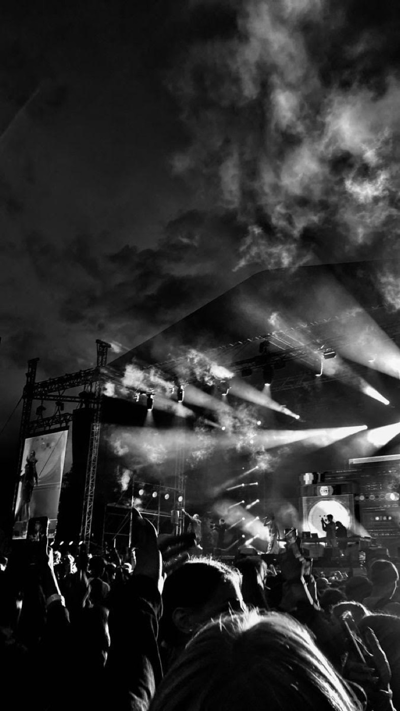 Black-and-white photograph of a concert stage lit by beams of light above a crowd.