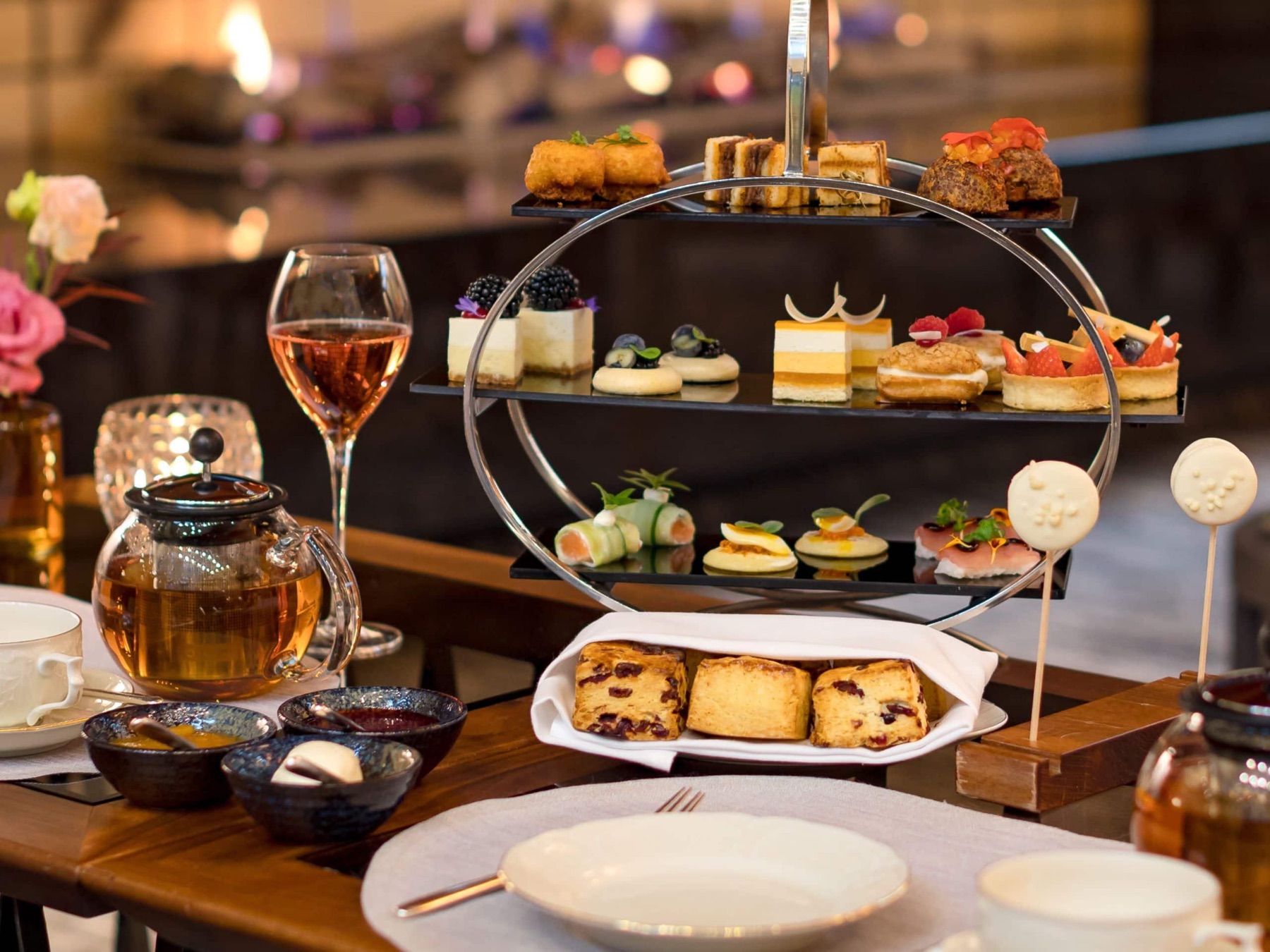 An elegant tiered afternoon-tea stand of pastries and savouries beside a glass of rosé and a pot of tea at Park Hyatt Zurich.
