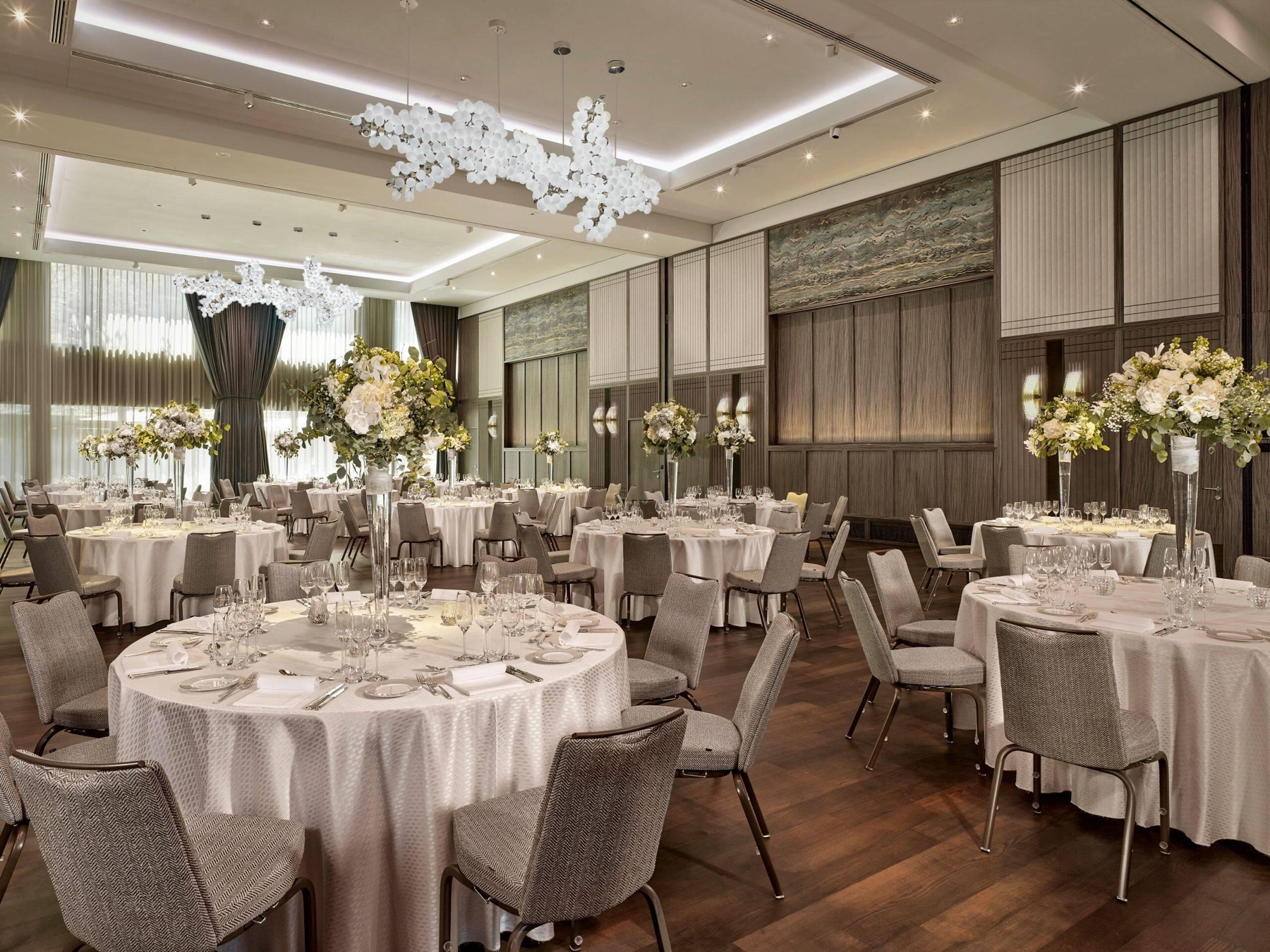 The Park Hyatt Zurich ballroom set for a gala — round tables in ivory linen with tall floral centrepieces beneath sculptural white-orchid chandeliers.