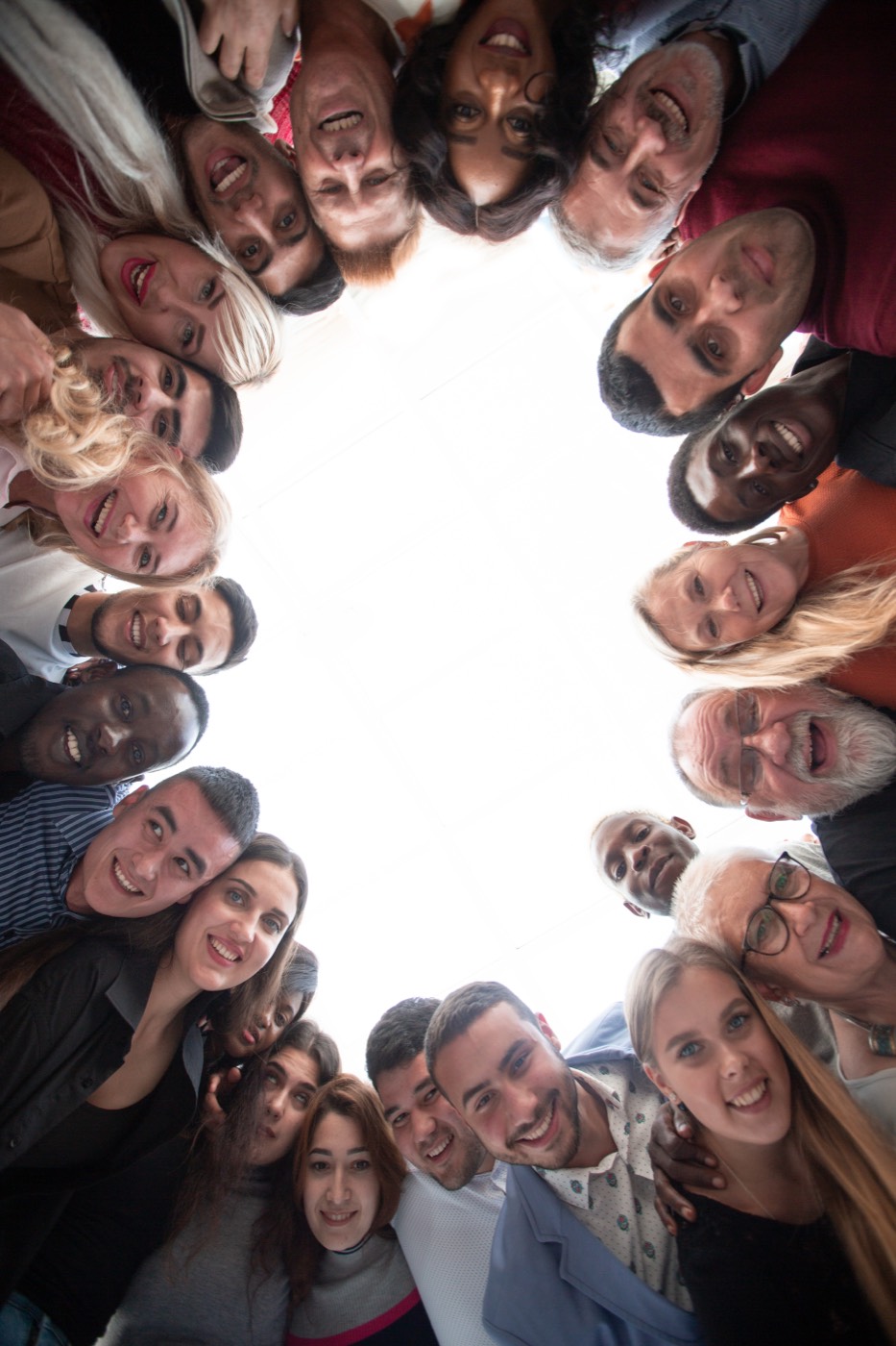 A circle of diverse people looking inward and smiling, seen from below.